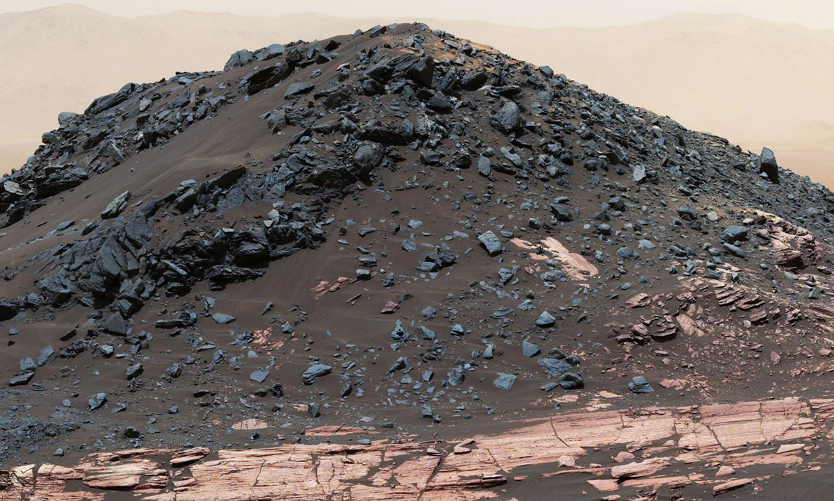 This dark mound, called "Ireson Hill," rises about 16 feet (5 meters) above redder layered outcrop material of the Murray formation on lower Mount Sharp, Mars, near a location where NASA's Curiosity rover examined a linear sand dune in February 2017.Researchers used the rover's Mast Camera (Mastcam) on Feb. 2, 2017, during the 1,598th Martian day, or sol, of Curiosity's work on Mars, to take the 41 images combined into this scene. The mosaic has been white-balanced so that the colors of the rock and sand materials resemble how they would appear under daytime lighting conditions on Earth. The view extends from west-southwest on the left to north-northwest on the right. The faint horizon in the distance beyond Ireson Hill is part of the rim of Gale Crater.  (NASA/JPL-Caltech/MSSS)