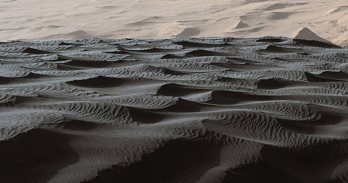 Two sizes of wind-sculpted ripples are evident in this view of the top surface of a Martian sand dune. Sand dunes and the smaller type of ripples also exist on Earth. The larger ripples -- roughly 10 feet (3 meters) apart -- are a type not seen on Earth nor previously recognized as a distinct type on Mars.The Mast Camera (Mastcam) on NASA's Curiosity Mars rover took the multiple component images of this scene on Dec. 13, 2015, during the 1,192nd Martian day, or sol, of the rover's work on Mars. That month, Curiosity was conducting the first close-up investigation ever made of active sand dunes anywhere other than Earth.The larger ripples have distinctive sinuous crest lines, compared to the smaller ripples.The location is part of "Namib Dune" in the Bagnold Dune Field, which forms a dark band along the northwestern flank of Mount Sharp.The component images were taken in early morning at this site, with the camera looking in the direction of the sun. This mosaic combining the images has been processed to brighten it and make the ripples more visible. The sand is very dark, both from the morning shadows and from the intrinsic darkness of the minerals that dominate its composition.  (NASA/JPL-Caltech/MSSS)